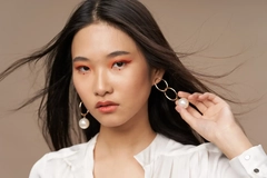 Image A woman wearing makeup and pulling at her earing.