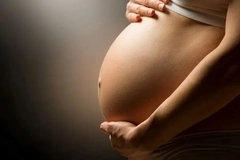 A pregnant women holding her tummy in a darkened room.
