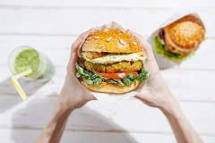 Image vegan burger in hands of a woman with a drink in the background