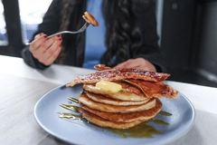 a man's hand holding a piece of cultivated bacon on a fork with a pancakes on a plate