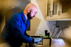 Image A person wearing safety glasses and gloves looking at a computer.