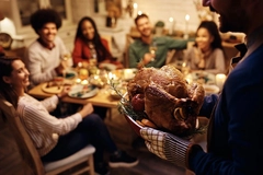 Image man's hand holding roasted turkey with friends waiting at dinner table