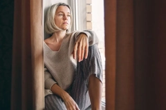 Image A woman sitting on the window sill looking outside.