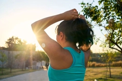 Image Young Latin sportswoman tying hair with glucose sensor or monitor at sunset in park.