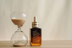 Image Estee lauder serum next to a hourglass.