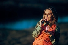 Image A woman prepares to eat a gummy supplement while standing in an open field.