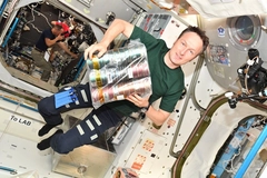 Image male astronaut inside ISS wearing tshirt and pants holding food cans