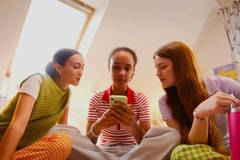 Image Three young girls sitting together looking at a phone.