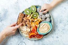 Image two hands picking up healthy bars and balls from a round plate