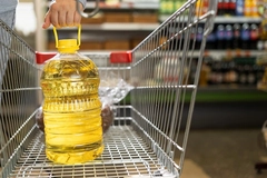 woman's hand putting bottle of yellow oil in shopping cart
