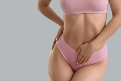 A woman wearing a pink underwear and bra set and putting her hand on her stomach.