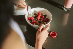 Image woman pours milk over bowl containing cereal and berries