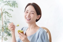 Happy woman eats gold kiwi with spoon