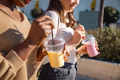 Image hands of two women walking with smoothie in transparent cups
