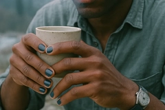 Image A man with painted nails holding a cup.