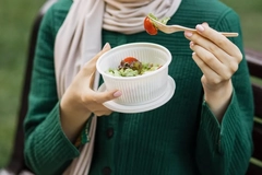 Image A person holding a plastic bowl of salad and eating it with a plastic fork
