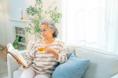 Happy Asian senior woman wearing glasses reading a book with drinking a cup of tea Happy Asian senior woman wearing glasses reading a book with drinking a cup of tea