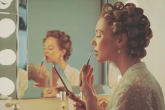 Image A woman wearing curlers putting on lipstick with a lip brush.