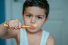 A little boy holding up a toothbrush with a small amount of toothpaste on it.