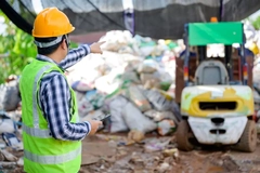 A person in a hard hat pointing at a garbage dump