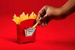 A hand dipping a fry on a container of french fries