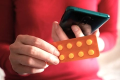 Image A close-up of a person holding a smart phone and a blister pack for pills