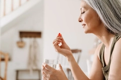 A woman takes a supplement while sitting on the couch.