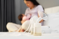 Image Breast milk in bottles of electric breast pumping set on bed with mother breastfeeding newborn baby background