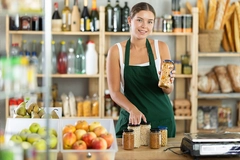 Image friendly girl seller behind a store counter offering to buy canned beans and legumes