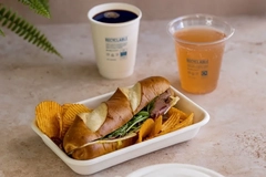 A sandwich and chips in a container with two cups of drinks on the table.