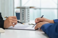 Image Two hands holding pens and one signing a contract.