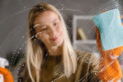 Image A girl wiping glass with cleaner.