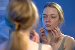 Image young woman looking unhappily in mirror