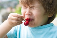 Image boy eating cherries and making an unpleasant face