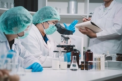 A food scientist looks thorugh microscope while 2 researchers take notes