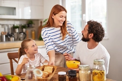 Image mother, father, daughter eating breakfast on table with cereal