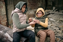 Image Two hungry girls from refugee camp sharing peach while sitting on ruins of building