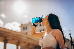 Image A woman drinks a supplement shake from a cup in the sun.