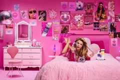 Image Woman with voluminous hair lying on bed talking into phone in a hot pink room with posters on walls including John Freida Frizz-Ease product poster.