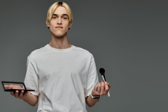Image A man holding a makeup palette and a makeup brush.