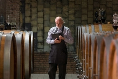 A winery expert inspects data on a tablet while surrounded by oak barrels.