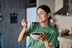 Image young woman preparing and eating breakfast, drinking juice in the kitchen
