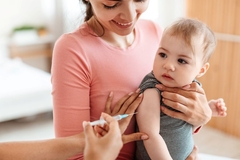 Doctor giving shot to little baby on arm, sitting on mothers lap