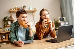 Gen Alpha children eating burgers looking at laptop screen.