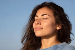 Image Young woman in golden hour sunlight eyes closed taking a deep peaceful breath under a clear blue sky