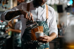 male barista adding milk to coffee in cafe