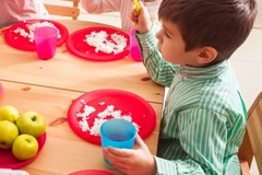 Image A group of kids sitting at a table eating from plastic plates and cups