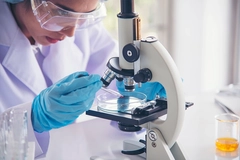 Image scientist in lab gear dropping liquid under microscope