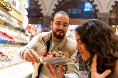 Image A salesman in the grand bazaar hold up dried tea leaves for a woman to smell