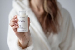 A hand holding a Olaplex hair care product.